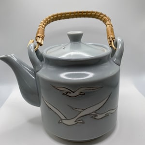 May include: A gray ceramic teapot with a woven bamboo handle and a design of white seagulls in flight.