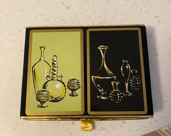 Könnte beinhalten: Eine Vintage-Box in Schwarz und Gold mit zwei Tafeln, die stilisierte Abbildungen von Flaschen und Gläsern zeigen. Eine Tafel ist hellgrün, die andere ist schwarz. Die Box hat einen goldfarbenen Rand und eine kleine goldene Zuglasche.