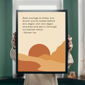 Könnte beinhalten: Ein beiger druckbarer Poster mit einem Zitat von Harper Lee: "Wahrer Mut ist, wenn man weiß, dass man geschlagen ist, bevor man überhaupt anfängt, aber man fängt trotzdem an und zieht es durch, egal was passiert." Der Poster zeigt einen Sonnenuntergang über einer Wüstenlandschaft in Orange- und Brauntönen.