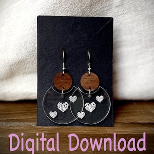 May include: A pair of clear acrylic earrings with a brown wooden circle and white heart designs. The earrings are hanging from silver hooks.