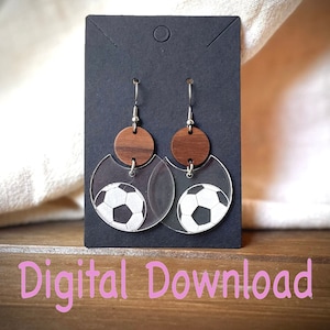 May include: A pair of clear acrylic earrings with a wood circle and a soccer ball design. The earrings are hanging from silver hooks.