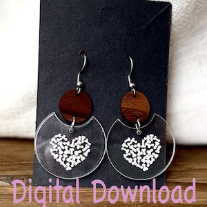 May include: A pair of clear acrylic earrings with a white heart design and a brown wooden accent. The earrings are hanging from a black display card.