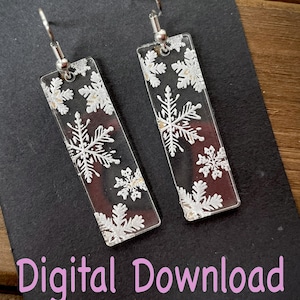May include: A pair of clear acrylic earrings with a snowflake design. The earrings are rectangular in shape and have silver hooks.
