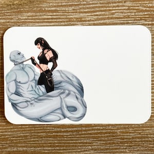 May include: A white rectangular sticker featuring an illustration of a muscular, pale-skinned figure with a snake-like tail, held by a woman with black hair and clothing. The artwork is detailed with shading and highlights.