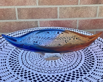 May include: A large, blue and brown glass bowl with a unique, organic shape. The bowl is sitting on a white crocheted doily.