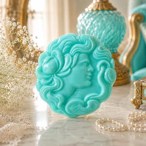 Peut inclure: Une pièce décorative ronde turquoise représentant un profil classique en relief. La pièce est entourée de cheveux fluides et d'éléments floraux. L'image comprend également un collier de perles, une boîte décorative et une lampe turquoise.