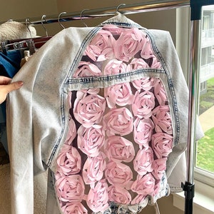 May include: A light blue denim jacket with a sheer panel on the back featuring pink 3D fabric roses.