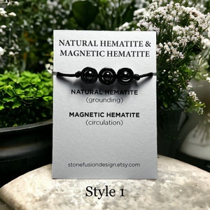 May include: A black hematite bracelet featuring three polished, round beads on a black cord. The bracelet is presented on a white card with text: "NATURAL HEMATITE & MAGNETIC HEMATITE". The card also includes the text "Style 1".