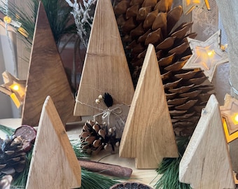 May include: Five wooden Christmas tree ornaments in various sizes, made from natural wood with a rustic finish. The trees are arranged on a table with pine needles, cinnamon sticks, and other natural decorations.