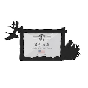 May include: Black metal photo frame with a rustic wood design. The frame features a silhouette of a flock of geese flying and a couple of birds in a nest. The frame is 3 1/2 inches by 5 inches and is made in the USA.