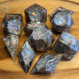 May include: Set of eight iridescent dice with a black and gold speckled pattern. The dice are made of resin and have a clear, translucent finish.