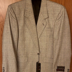 May include: A tan and black plaid blazer with a black interior lining. The blazer has a notched lapel, two front pockets, and three buttons on each cuff. A black tag hangs from the blazer.