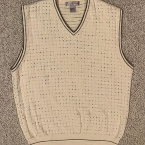 May include: Cream-colored, sleeveless sweater vest with a V-neck and a textured, woven pattern. The vest has a ribbed hem and trim in a darker neutral color. The tag reads "Express Linen".