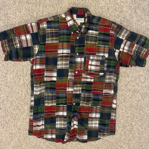 May include: A short-sleeved patchwork shirt with a button-down collar and a chest pocket. The shirt features a variety of plaid patterns in shades of red, green, blue, and white. The brand "ORVIS" is visible on the collar.