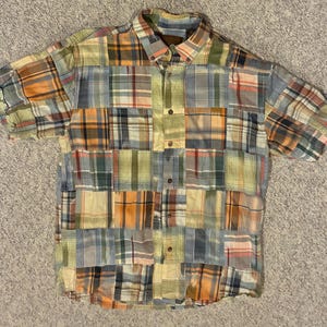 May include: A short-sleeved button-down shirt with a patchwork design. The shirt features a variety of plaid patterns in shades of orange, green, blue, and yellow. The shirt has a collared neckline and button closures down the front.