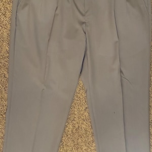 Puede incluir: Pantalones de vestir azul claro con pliegues, cierre de botón y dos bolsillos delanteros. Los pantalones tienen un dobladillo con vuelta y una etiqueta adjunta. Los pantalones están hechos de una tela lisa y resistente a las arrugas.