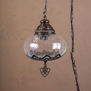 May include: A clear glass pendant light with a decorative metal cap and base. The glass globe has a patterned design around the bottom. The light fixture is suspended by a dark wire and chain.