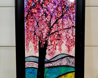May include: Framed abstract painting of a pink tree with a black trunk and branches against a blue and green landscape. The painting is done in a style reminiscent of stained glass.