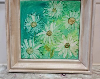 May include: A framed artwork featuring a floral design. The artwork showcases white daisy-like flowers with yellow centers against a green background. The frame is a light, neutral color, enhancing the artwork's visual appeal. The piece is a square format.