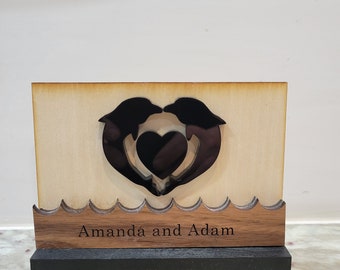 May include: Wooden plaque with two dolphins forming a heart shape with the text "Amanda and Adam" below.