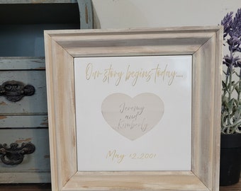 May include: A framed white tile with gold lettering that reads "Our story begins today..." with a heart shape that says "Jeremy and Kimberly" and the date "May 12, 2001".