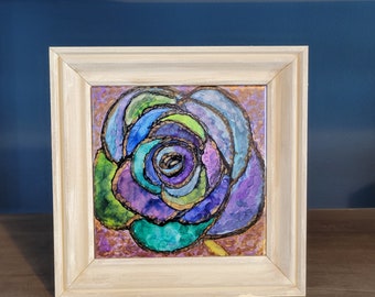May include: A framed painting of a colorful abstract rose with shades of purple, blue, green, and gold. The rose is painted in a style reminiscent of stained glass.