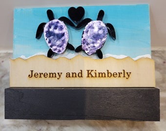 May include: Wooden sign with two purple sea turtles holding a black heart. The sign says "Jeremy and Kimberly" on the bottom.