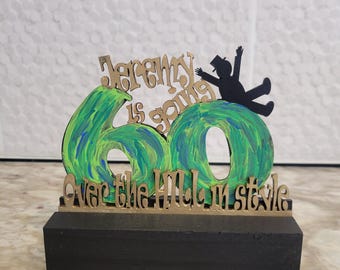 May include: A green and gold wooden sign with the text "Jeremy is going 60 over the hill in style" and a silhouette of a person going over a hill.