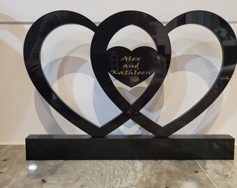 May include: Black acrylic heart-shaped wedding or anniversary decor with a smaller heart in the center. The smaller heart has the text "Alex and Kathleen" inscribed in gold.