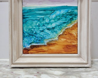 May include: A framed painting of an ocean scene with turquoise blue waves crashing on a sandy beach. The painting has a light brown frame.