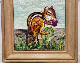 May include: A framed painting of a chipmunk eating a purple flower. The chipmunk is brown and white with a bushy tail. The background is a light blue and green watercolor wash.