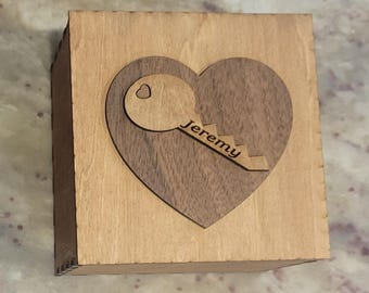 May include: A wooden box with a heart-shaped inlay. The inlay is made of a darker wood and features a key with the name "Jeremy" engraved on it.