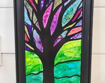 May include: A framed abstract painting of a tree with a black trunk and colorful branches. The background is a mix of green, blue, and purple.