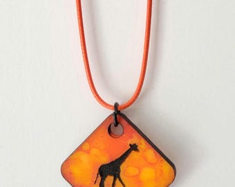 May include: A wooden pendant necklace featuring a black silhouette of a giraffe against an orange and yellow background. The pendant is diamond-shaped with a black border and hangs from an orange cord.
