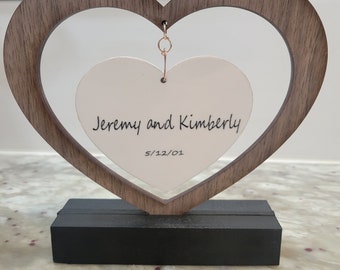 May include: A wooden heart-shaped frame with a smaller heart-shaped card inside. The card is white and has the text "Jeremy and Kimberly 5/12/01" written on it.