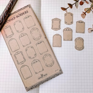 May include: Kraft paper labels with ornate borders, featuring a vintage design. The sheet of labels and individual labels are arranged on a grid paper background. The text "ADORNED BORDERS" and "GOOSE DEVIL" are visible.