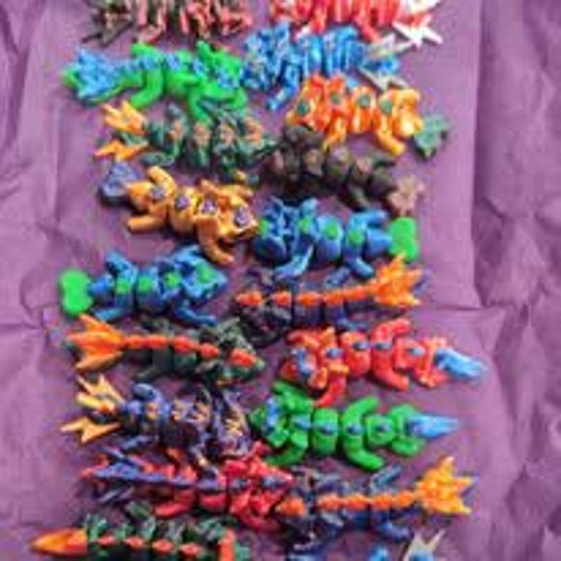 K&ouml;nnte beinhalten: Eine Sammlung von beweglichen Kunststoff-Drachenfiguren in verschiedenen Farben wie Gr&uuml;n, Blau, Orange, Rot und Schwarz. Jeder Drache hat einen segmentierten K&ouml;rper, einen detaillierten Kopf und einen Schwanz, angeordnet in Reihen auf einer violetten Oberfl&auml;che.