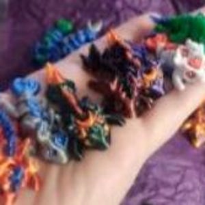 K&ouml;nnte beinhalten: Eine Sammlung kleiner, mehrfarbiger Drachenfiguren mit komplexen Schuppen und Stacheln in verschiedenen Blau-, Orange-, Gr&uuml;n-, Schwarz- und Wei&szlig;t&ouml;nen. Diese fantastischen Miniaturkreaturen werden zusammen pr&auml;sentiert und zeigen vielf&auml;ltige Farbmuster.