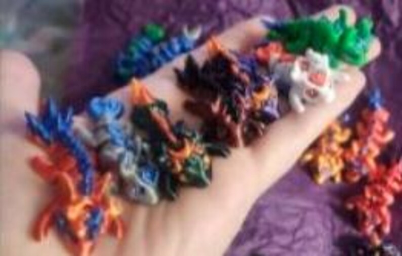 K&ouml;nnte beinhalten: Eine Sammlung kleiner, mehrfarbiger Drachenfiguren mit komplexen Schuppen und Stacheln in verschiedenen Blau-, Orange-, Gr&uuml;n-, Schwarz- und Wei&szlig;t&ouml;nen. Diese fantastischen Miniaturkreaturen werden zusammen pr&auml;sentiert und zeigen vielf&auml;ltige Farbmuster.