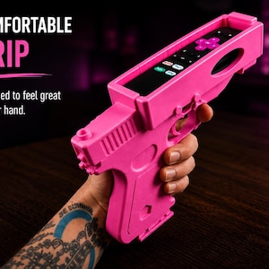K&ouml;nnte beinhalten: Ein leuchtend pinkfarbener Fernbedienungshalter aus Kunststoff in Pistolenform mit einem rechteckigen Schlitz an der Oberseite f&uuml;r eine schwarze Fernbedienung. Der Text 3 COMFORTABLE GRIP und Designed to feel great in your hand ist aufgedruckt.
