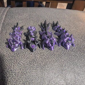 K&ouml;nnte beinhalten: Vier bewegliche Drachenfiguren in einer metallisch violetten und schwarzen Farbgebung. Jeder Drache verf&uuml;gt &uuml;ber einen segmentierten K&ouml;rper, einen detaillierten Kopf mit H&ouml;rnern und einen Schwanz. Die Figuren sind in einer Reihe angeordnet.