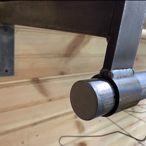 May include: Close-up of a metal shelf bracket with a round, silver end cap. The bracket is attached to a wooden wall.