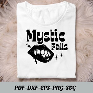 Może przedstawiać: Biała koszulka z czarnym napisem "Mystic Falls" i czarną ilustracją ust wampira z kłami.