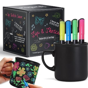 May include: Black ceramic mug with a chalkboard surface. The mug is part of a set that includes four colorful markers. The box for the set features the text "Sip & Sketch DoodleMug" and a butterfly design.