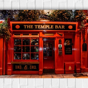May include: Exterior view of The Temple Bar, a pub with a red facade and black signage. The sign reads "THE TEMPLE BAR" in gold lettering. The windows are decorated with snowflakes. The pub is illuminated at night.