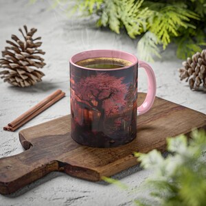 May include: A pink ceramic mug with a black and white image of a cherry blossom tree and a Japanese-style building. The mug is filled with a dark liquid and steam is rising from it.