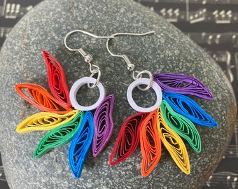 May include: Rainbow paper quilled earrings with silver hooks. The earrings are shaped like a sunburst with each ray of the sun a different color of the rainbow.