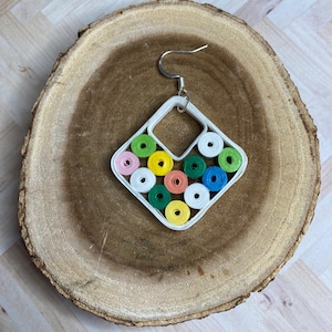 May include: White diamond-shaped paper quilling earrings with a silver hook. The earrings are decorated with colorful paper rolls in shades of pink, green, yellow, orange, and white.