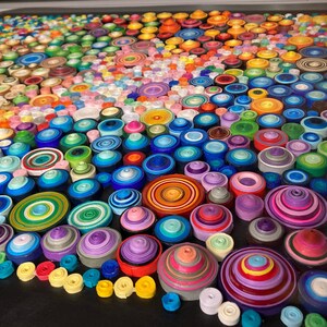 May include: A colorful mosaic art piece made of rolled paper circles. The circles are arranged in a circular pattern, creating a swirling effect. The colors are vibrant and varied, including red, orange, yellow, green, blue, purple, and pink.