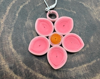 May include: A flower-shaped pendant crafted from coiled paper strips in shades of pink and orange. The design features five teardrop-shaped pink petals surrounding a central orange circular core, attached to a silver-toned metal lever-back earring hook.